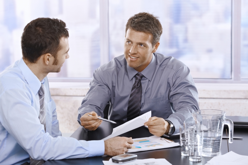 Happy businessmen discussing business report sitting at meeting table in office.